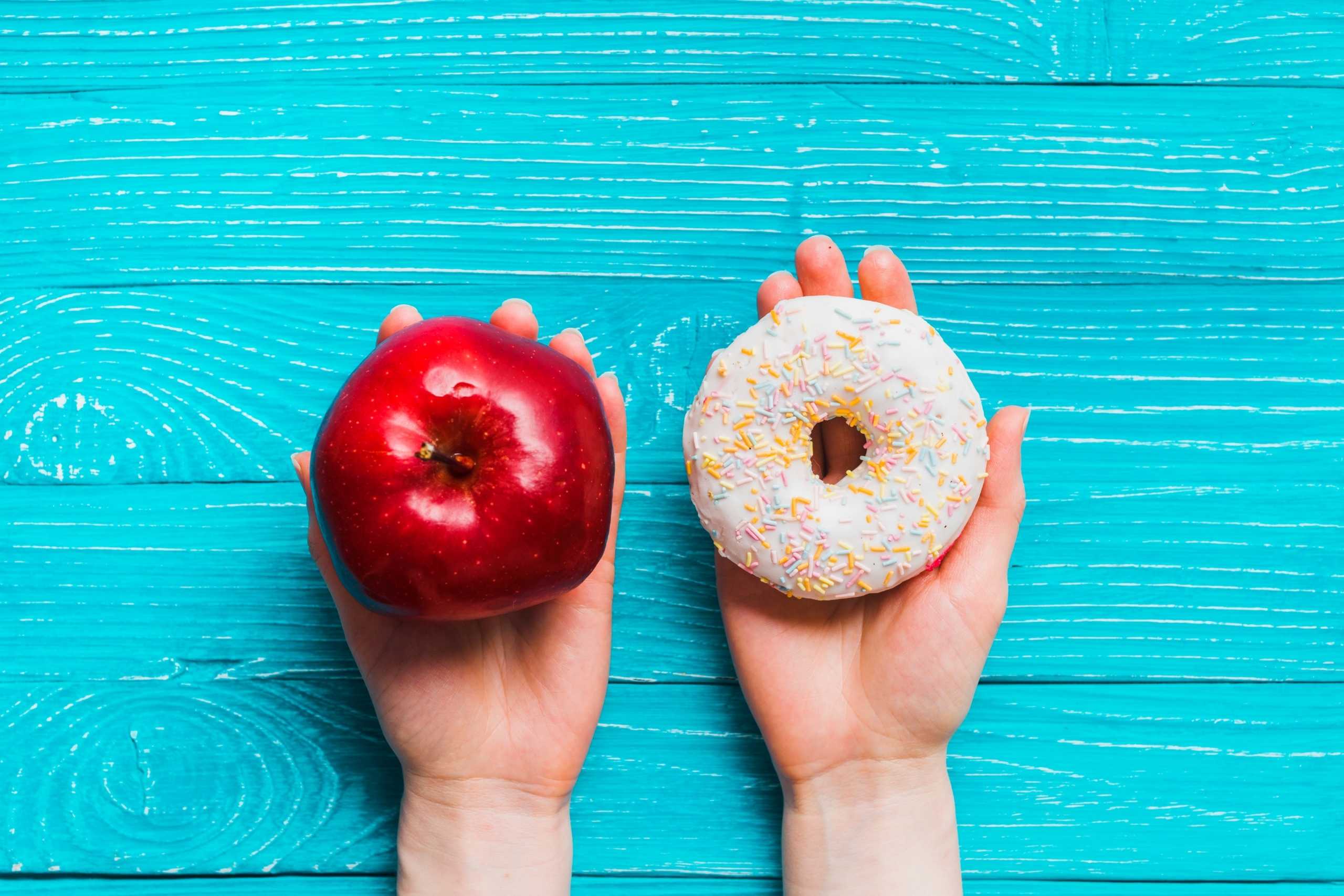 Manos sosteniendo una manzana y con la otra una donut
